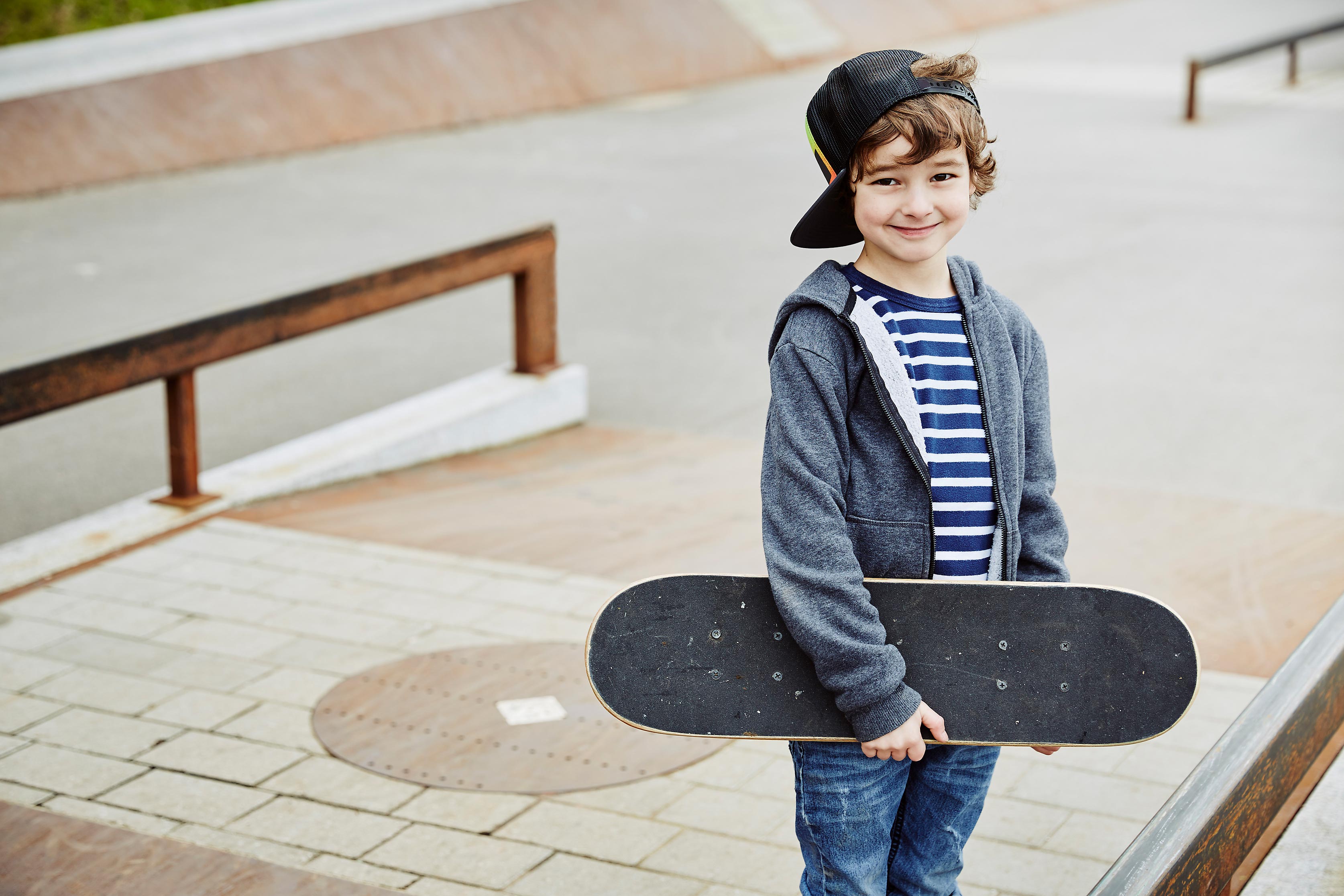 Kleiner Junge mit Skateboard in der Hand grinst freundlich. Symbol für unsere uniVersa Unfallversicherung speziell für Kinder