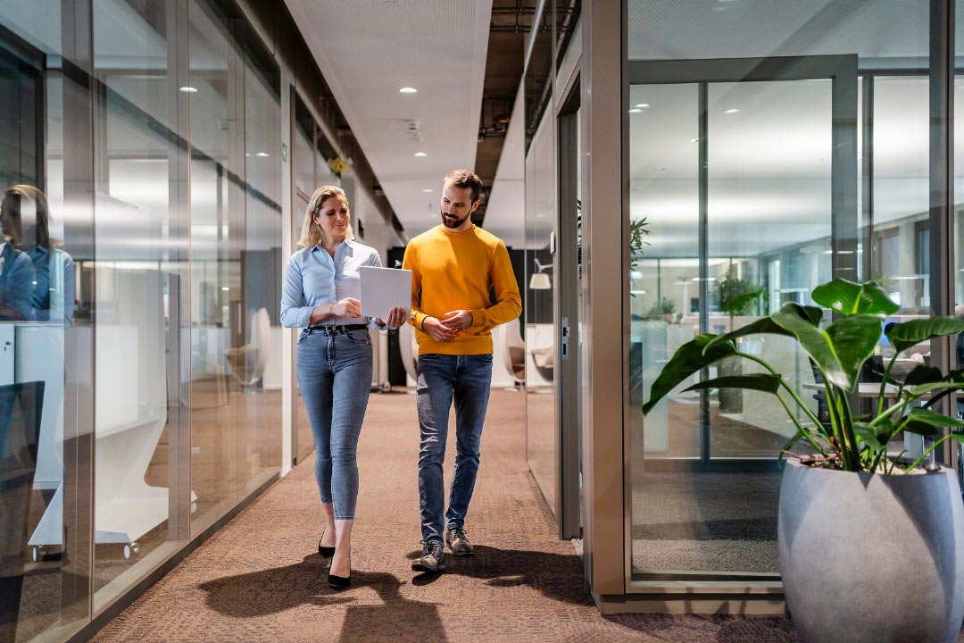 Frau und Mann laufen nebeneinander den Bürogang entlang. Werden Sie Teil des Teams im Bereich Vertrieb