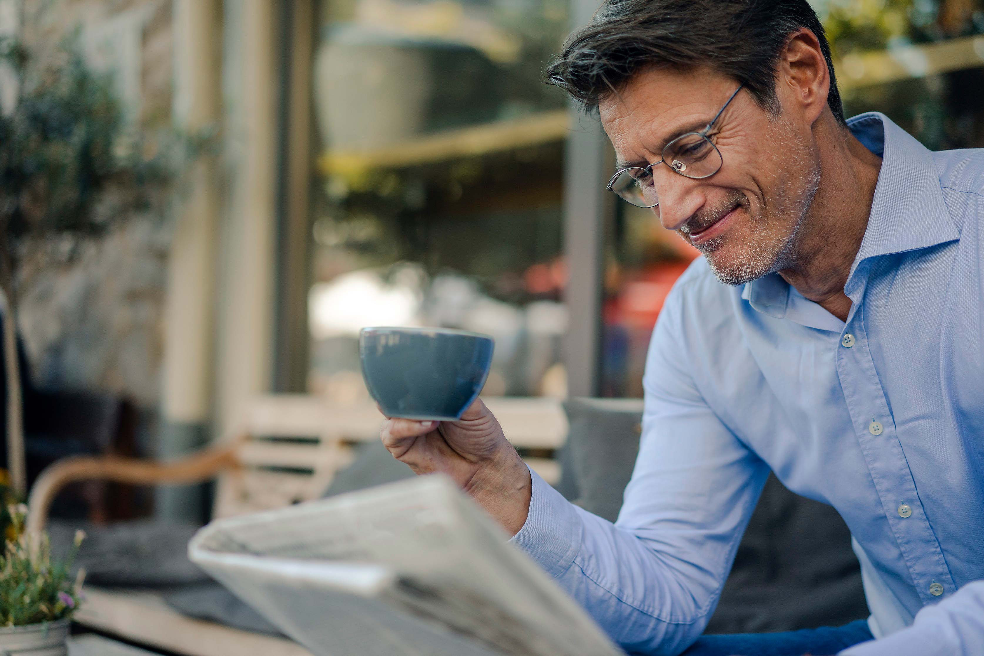 Mann der bei einer Tasse Kaffee die Zeitung liest. Symbol für unsere uniVersa Pressemitteilungen